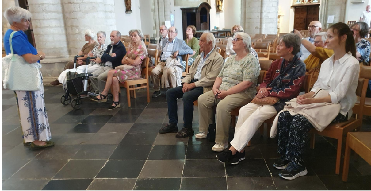 Deelnemers aan de rondleiding in de kerk, aandachtig luisterend naar Kathleen Smolders